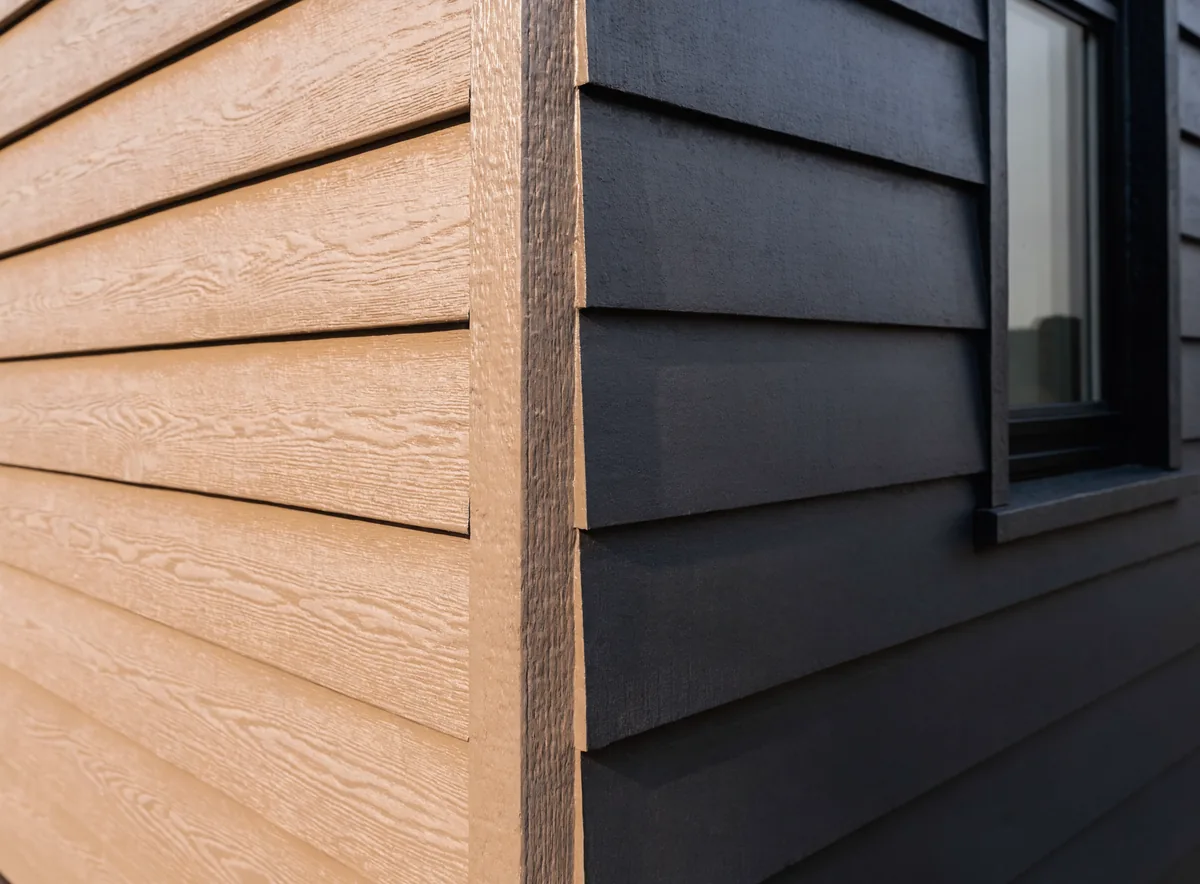 Corner detail where warm woodgrain Hardie lap siding meets a dark flat-panel section